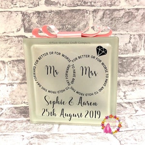 Op de afbeelding: Een witte glazen blok met een roze lint eromheen gebonden. De blok heeft zwarte tekst die luidt "Mr. & Mrs.  To have and to hold from this day forward for better or for worse." De namen "Sophie & Aaron" en de datum "25th August 2019" staan ook op de blok gedrukt.