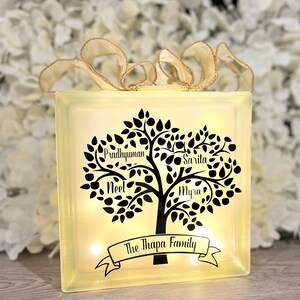 Op de afbeelding: Een lichtgevend glazen blok met een zwart silhouet van een stamboom. De namen "Pradyuman", "Sarita", "Neel" en "Myra" staan op de takken. De tekst "The Thapa Family" staat op een banner onderaan de boom.