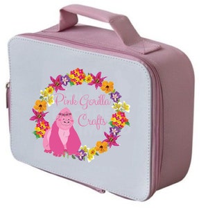 Pode incluir: Uma lancheira rosa com fecho de correr e al&ccedil;a. A lancheira tem um painel frontal branco com um design de coroa de flores e o texto "Pink Gorilla Crafts".