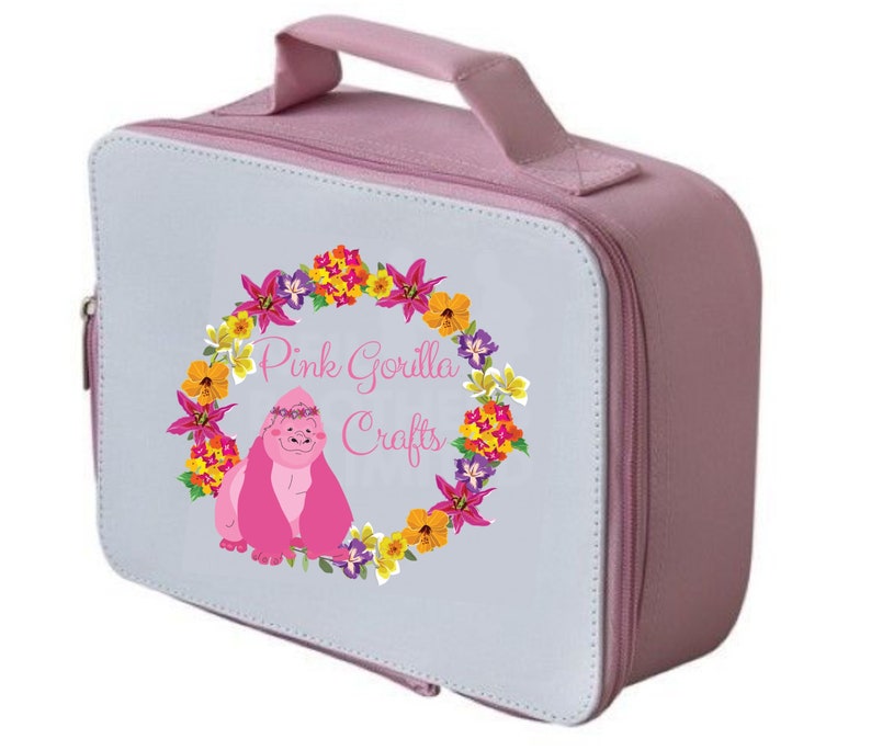 Pode incluir: Uma lancheira rosa com fecho de correr e al&ccedil;a. A lancheira tem um painel frontal branco com um design de coroa de flores e o texto "Pink Gorilla Crafts".