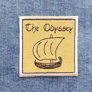 May include: Embroidered patch featuring the text "The Odyssey" above a line drawing of a sailboat. The patch has a yellow background with black and white details. The patch is square and set against a blue denim background.