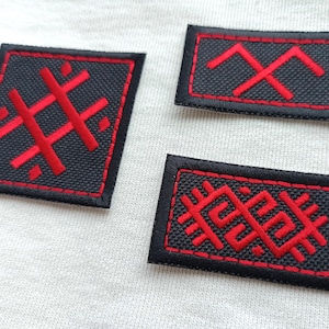 May include: Three black embroidered patches with red geometric designs. The patches have a black border and are rectangular and square shaped. The patches are on a white surface.