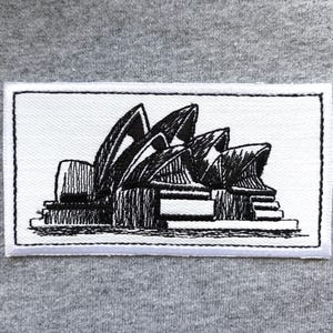 May include: Embroidered patch depicting the Sydney Opera House in black and white. The rectangular patch has a white background and a black border, showcasing the iconic architectural design.