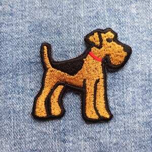 May include: Embroidered patch featuring a stylized dog with brown and black fur, a red collar, and black outline. The patch is on a blue denim background. The dog is standing, with its tail up.