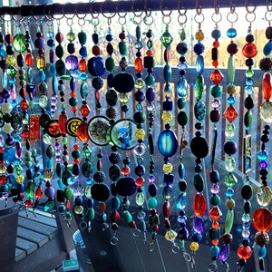 May include: A colorful beaded curtain with various shapes and sizes of beads, including round, square, and oval. The beads are made of glass and have a variety of colors, including red, blue, green, yellow, and purple. The curtain is hanging from a metal rod and is suspended in front of a window.
