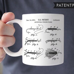 Pode incluir: Caneca de cerâmica branca com uma ilustração em preto e branco de uma patente para moscas de pesca artificiais. O número da patente é 2.533.523 e a data é 12 de dezembro de 1950.