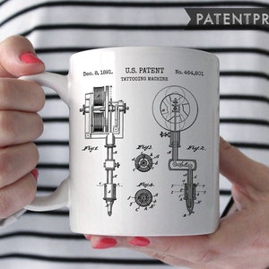 Pode incluir: Caneca de cerâmica branca com uma ilustração em preto e branco de uma patente de máquina de tatuagem. A patente é intitulada "U.S. Patent Tattooing Machine" e o número da patente é "No. 464,801". A data da patente é "Dec. 8, 1891".