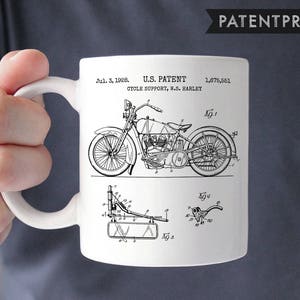 Pode incluir: Caneca de cerâmica branca com uma imagem em preto e branco de um desenho de patente de motocicleta. A patente é para um suporte de ciclo, W.S. Harley, e foi apresentada em 3 de julho de 1928. O número da patente é 1,675,551.