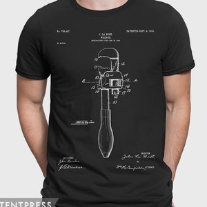 Puede incluir: Una camiseta negra con una ilustración blanca de un diseño de patente de llave inglesa. El número de patente es 738.457 y la fecha de la patente es el 8 de septiembre de 1903. El texto "J. La Burt Wrench" también está incluido en el diseño.