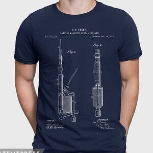 Puede incluir: Una camiseta azul marino con una impresión blanca de un dibujo de patente para un "Electro Magnetic Dental Plugger" de G.F. Green, patentado el 14 de diciembre de 1875. El dibujo muestra dos vistas diferentes del dispositivo, etiquetadas como "Fig. 1" y "Fig. 2".