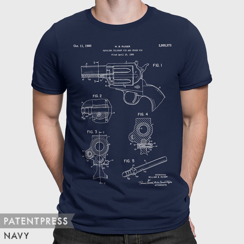 Puede incluir: Una camiseta azul marino con una impresi&oacute;n blanca de un dibujo de patente para un pasador de cilindro de rev&oacute;lver y un pasador transversal. El n&uacute;mero de patente es 2.955.373 y la fecha es el 11 de octubre de 1960. El inventor es William B. Ruger.