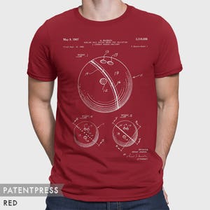 Pode incluir: Uma camiseta vermelha com uma estampa branca de um desenho de patente de bola de boliche. O n&uacute;mero da patente &eacute; 3.318.598 e a data da patente &eacute; 9 de maio de 1967. A patente &eacute; para uma bola de boliche que possui meios para indicar uma entrega correta com gancho.