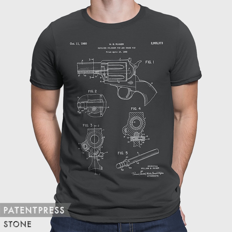 Puede incluir: Una camiseta negra con una impresi&oacute;n blanca de un dibujo de patente para un pasador de cilindro de rev&oacute;lver y un pasador transversal. El n&uacute;mero de patente es 2.955.373 y la fecha es el 11 de octubre de 1960. El inventor es William B. Ruger.