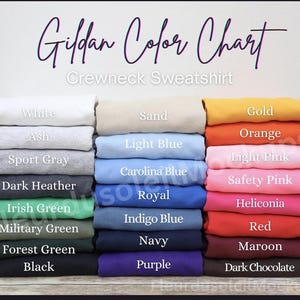 May include: A color chart for Gildan crewneck sweatshirts, showcasing a variety of colors. The chart displays folded sweatshirts in shades like white, ash, sport gray, dark heather, Irish green, military green, forest green, and black. Other colors include sand, light blue, Carolina blue, royal, indigo blue, navy, purple, gold, orange, light pink, safety pink, and red.