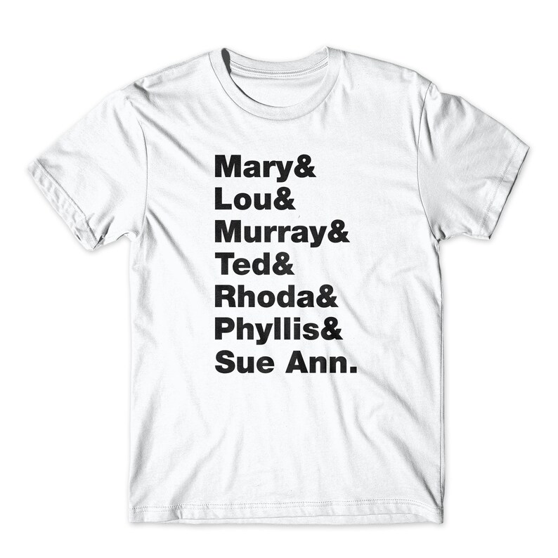 May include: White t-shirt with black text listing the names of the characters from the TV show "The Mary Tyler Moore Show": Mary, Lou, Murray, Ted, Rhoda, Phyllis, and Sue Ann.