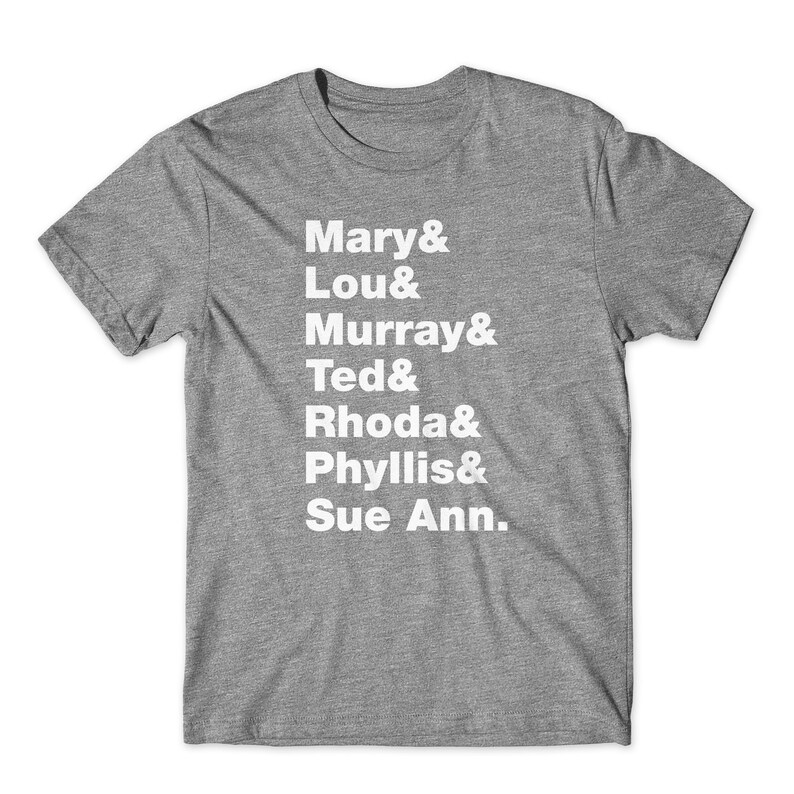 May include: A heather grey t-shirt with white text that reads "Mary & Lou & Murray & Ted & Rhoda & Phyllis & Sue Ann."