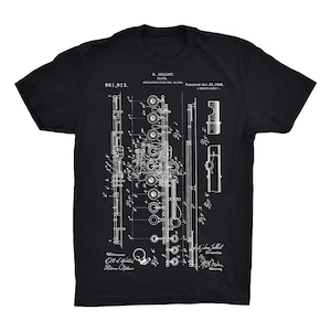 Pode incluir: Uma camiseta preta com uma estampa branca de um desenho de patente de flauta. O número de patente 901.913 é visível no topo do desenho. O texto "D. Julliot. Flauta. Patenteado em 20 de outubro de 1908." também é visível.