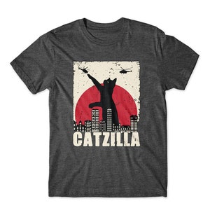 May include: A dark gray t-shirt with a vintage-style graphic of a black cat standing on a city skyline with the text "CATZILLA".