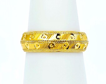 May include: A gold band ring with a textured design. The ring is on a white display stand.
