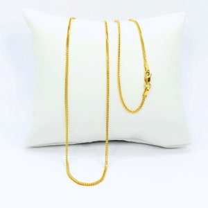 May include: A gold chain necklace with a box clasp. The chain is on a white pillow.