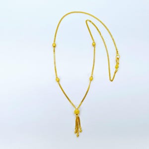 May include: A gold necklace with a tassel pendant and small round beads. The necklace is made of a delicate chain.