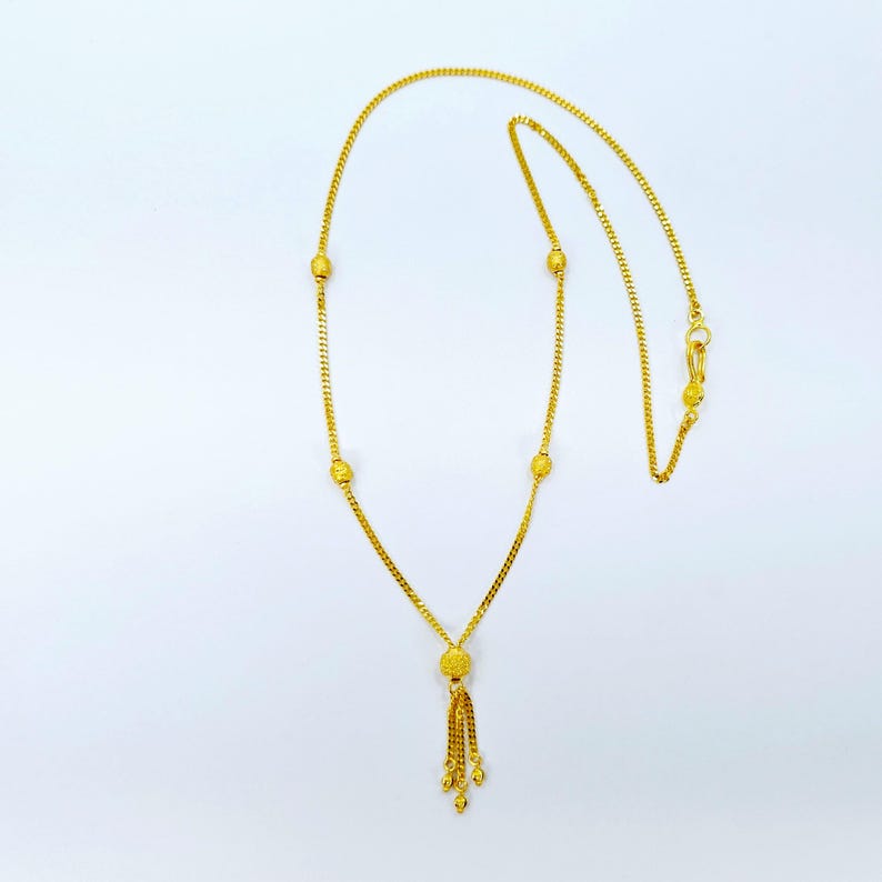 May include: A gold necklace with a tassel pendant and small round beads. The necklace is made of a delicate chain.