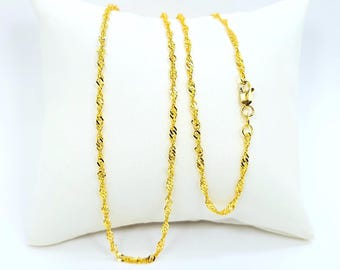 May include: A gold-colored necklace with a twisted rope design, resting on a white pillow. The necklace features a delicate chain with a secure clasp. The twisted pattern catches the light, creating a shimmering effect. The jewelry is displayed against a plain background.