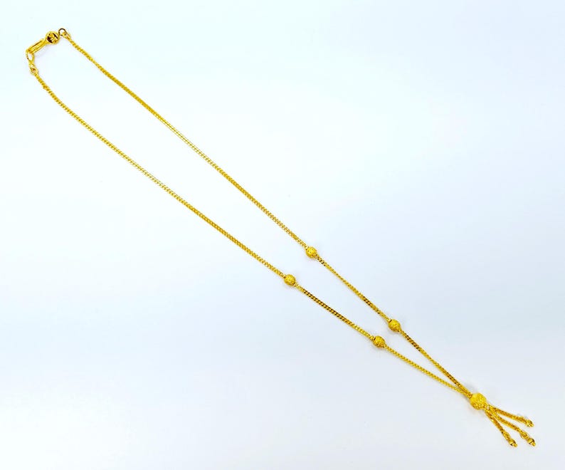 May include: A gold chain necklace with a tassel pendant. The chain has small round beads spaced along its length.
