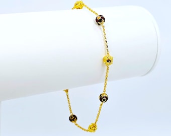 May include: A gold chain bracelet with five round red and gold beads. The beads have a textured surface and are connected by a delicate chain.