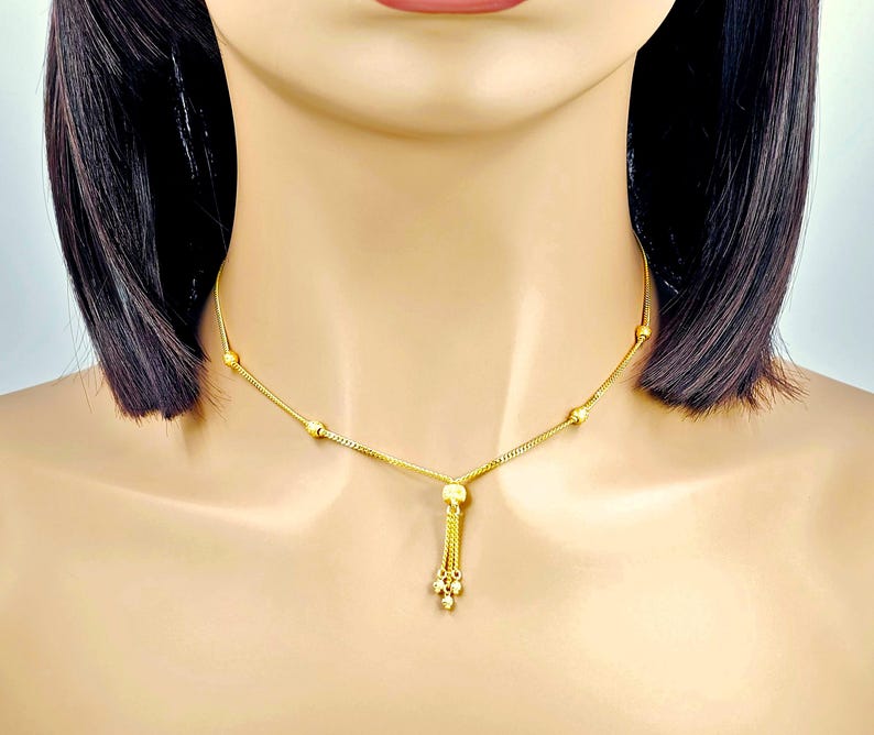 May include: A gold chain necklace with a tassel pendant. The chain has small round beads and the tassel is made of multiple small gold balls.