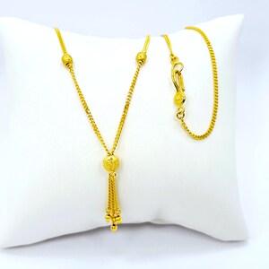 May include: A gold chain necklace with a tassel pendant. The chain has small round beads and the pendant has a larger round bead with a textured surface.