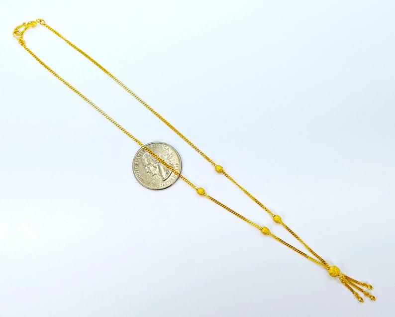May include: A gold chain necklace with a tassel pendant. The chain is adorned with small round beads.
