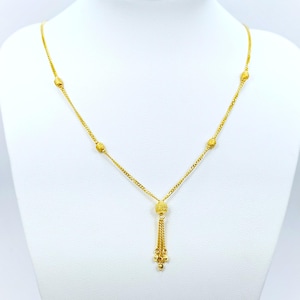 May include: A gold necklace with a tassel pendant and small round beads. The necklace is on a white background.