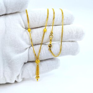 May include: A gold chain necklace with a tassel pendant. The chain has three small round beads and a clasp. The tassel is made of small gold beads.