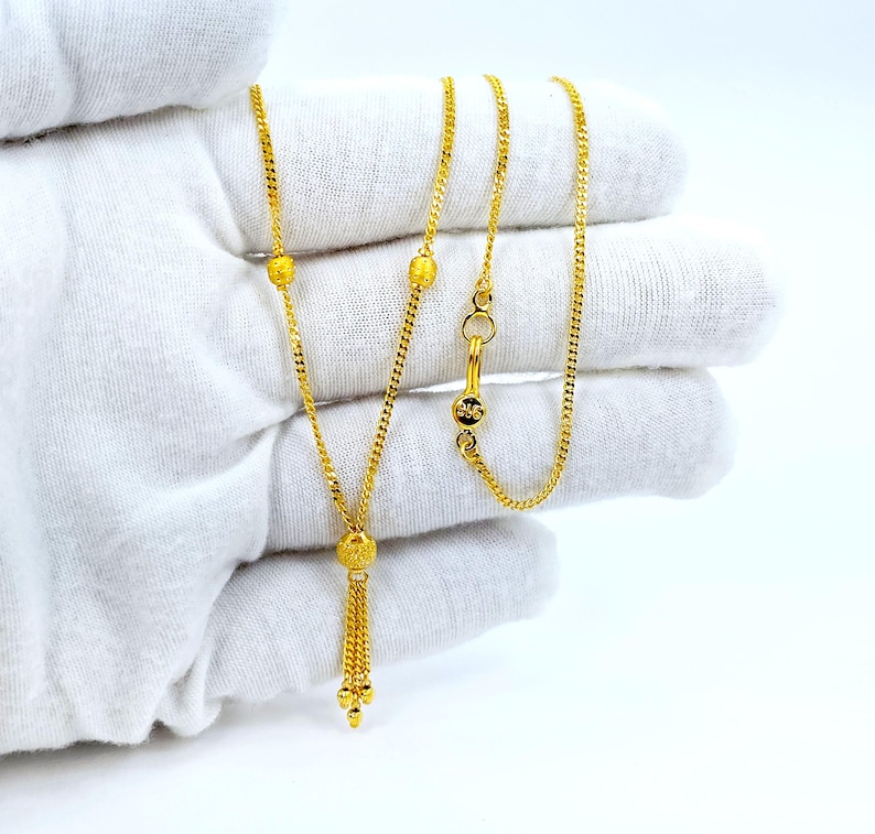 May include: A gold chain necklace with a tassel pendant. The chain has three small round beads and a clasp. The tassel is made of small gold beads.