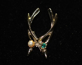 Puede incluir: Una pinza para el pelo de metal dorado con un diseño inspirado en la naturaleza. La pinza presenta una forma curvada con detalles delicados en forma de rama. Adornada con una perla, una gema verde y pequeños cristales transparentes, añade un toque de elegancia.