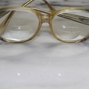 Può includere: Un paio di occhiali vintage con lenti rotonde trasparenti e una montatura in plastica marrone chiaro.