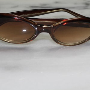 Peut inclure: Lunettes de soleil ovales en écaille de tortue brune avec des verres bruns.