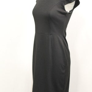 K&ouml;nnte beinhalten: Ein schwarzes Kleid mit kurzen &Auml;rmeln und einem runden Ausschnitt. Das Kleid ist figurbetont und hat eine knielange L&auml;nge.