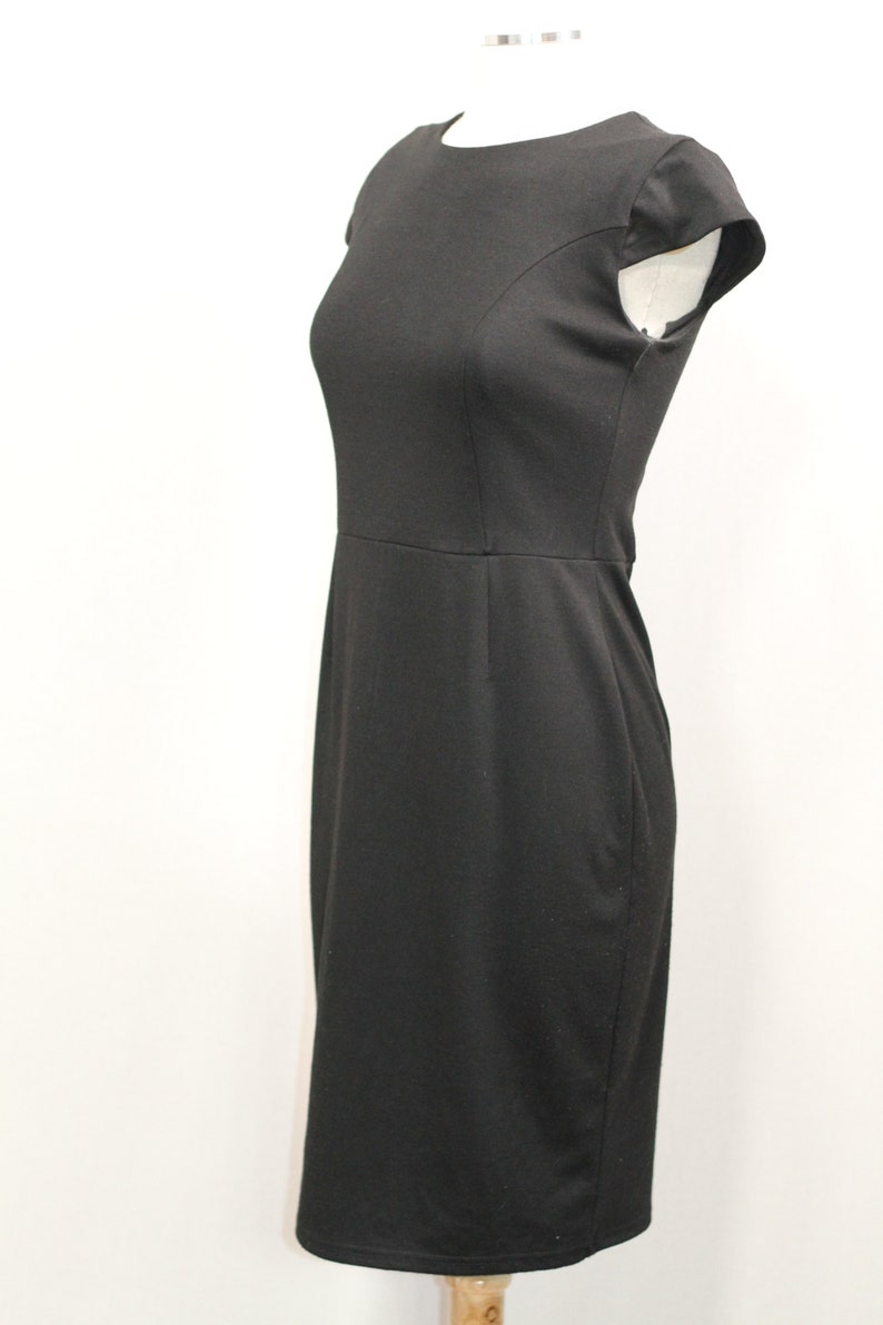 K&ouml;nnte beinhalten: Ein schwarzes Kleid mit kurzen &Auml;rmeln und einem runden Ausschnitt. Das Kleid ist figurbetont und hat eine knielange L&auml;nge.