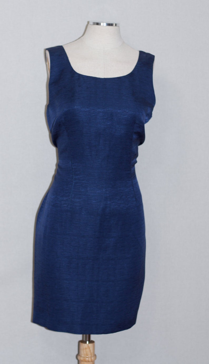 May include: A sleeveless, navy blue dress with a fitted silhouette. The dress has a scoop neckline and a smooth, textured fabric.