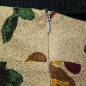 May include: A beige skirt with a zipper closure and a floral print featuring green, brown, red, and yellow colors.