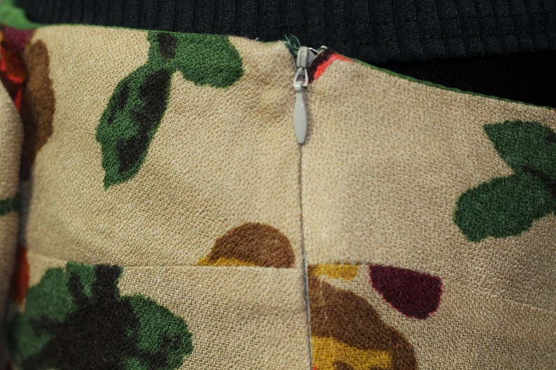 May include: A beige skirt with a zipper closure and a floral print featuring green, brown, red, and yellow colors.