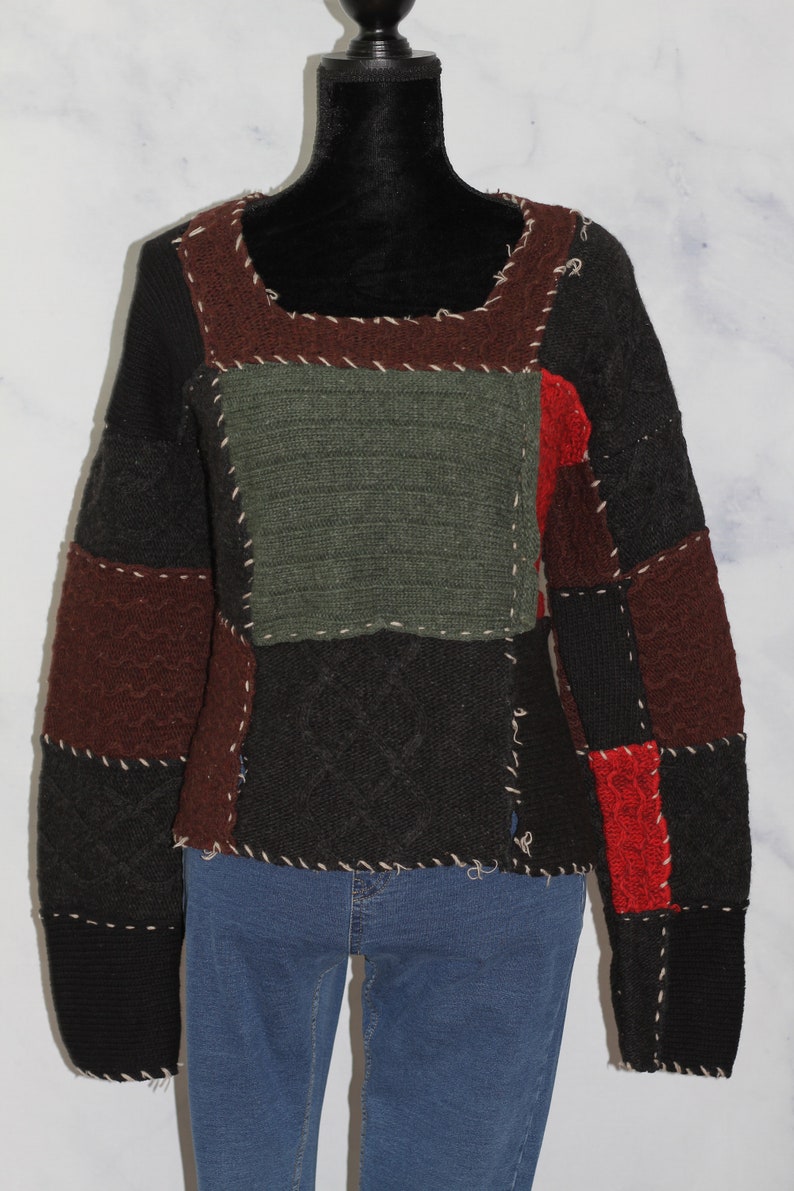 K&ouml;nnte beinhalten: Ein Patchwork-Pullover mit braunen, gr&uuml;nen, schwarzen und roten Strickpanels. Der Pullover hat einen Rundhalsausschnitt und lange &Auml;rmel.
