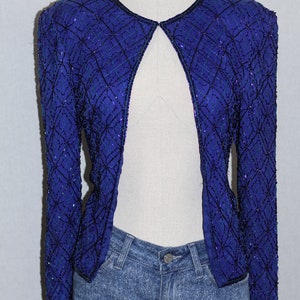 May include: A blue sequined jacket with a geometric pattern. The jacket is open in the front and has long sleeves.