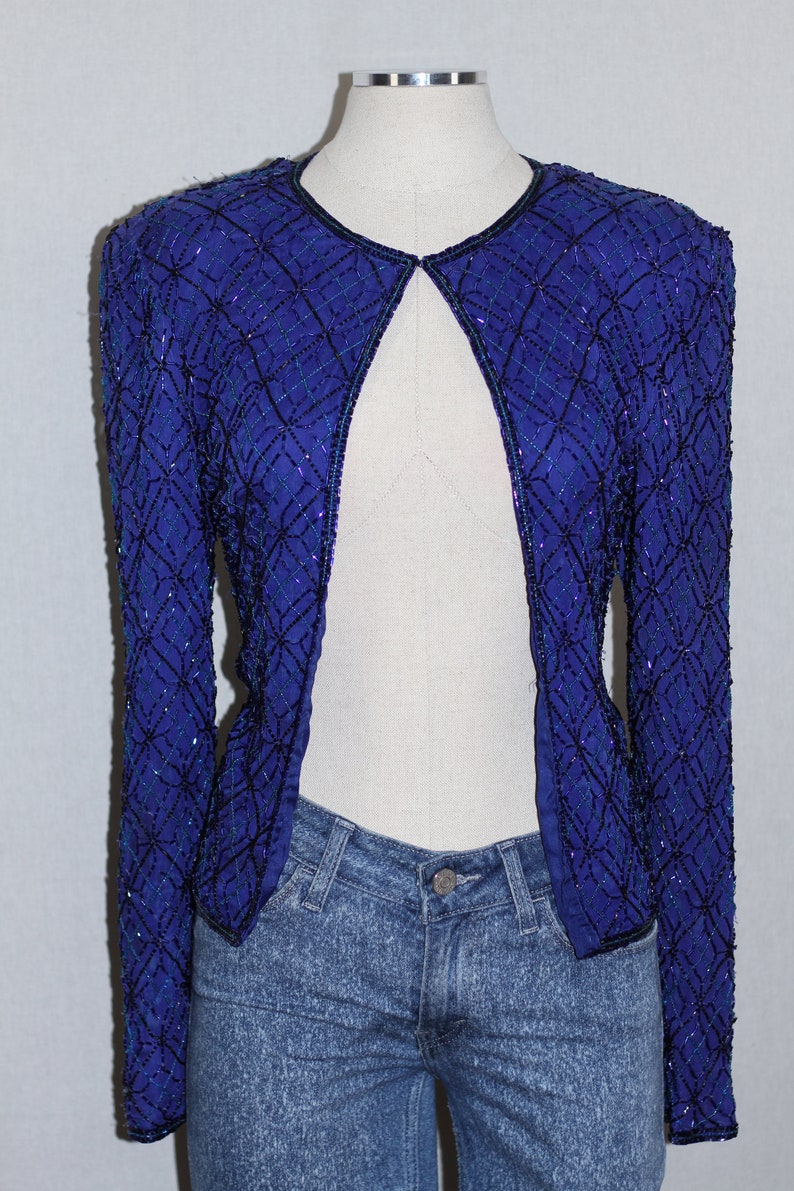 May include: A blue sequined jacket with a geometric pattern. The jacket is open in the front and has long sleeves.