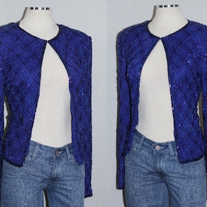May include: A royal blue sequined jacket with a V-neck and long sleeves. The jacket is open in the front and has a diamond pattern.