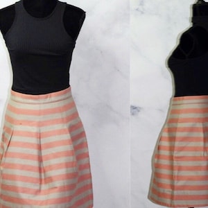 Puede incluir: Una falda de rayas rosa y blancas con un dise&ntilde;o plisado. La falda est&aacute; hecha de una tela sedosa y tiene una cintura ajustada.