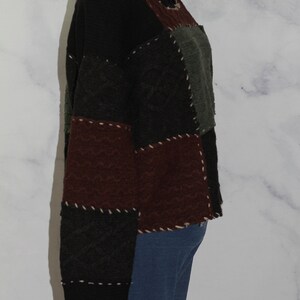 K&ouml;nnte beinhalten: Ein schwarzer, brauner und gr&uuml;ner Patchwork-Pullover mit Rundhalsausschnitt. Der Pullover besteht aus verschiedenen Texturen und hat einen einzigartigen, handgefertigten Look.