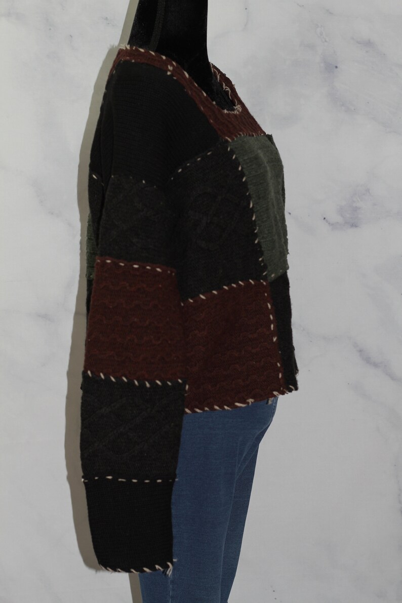 K&ouml;nnte beinhalten: Ein schwarzer, brauner und gr&uuml;ner Patchwork-Pullover mit Rundhalsausschnitt. Der Pullover besteht aus verschiedenen Texturen und hat einen einzigartigen, handgefertigten Look.